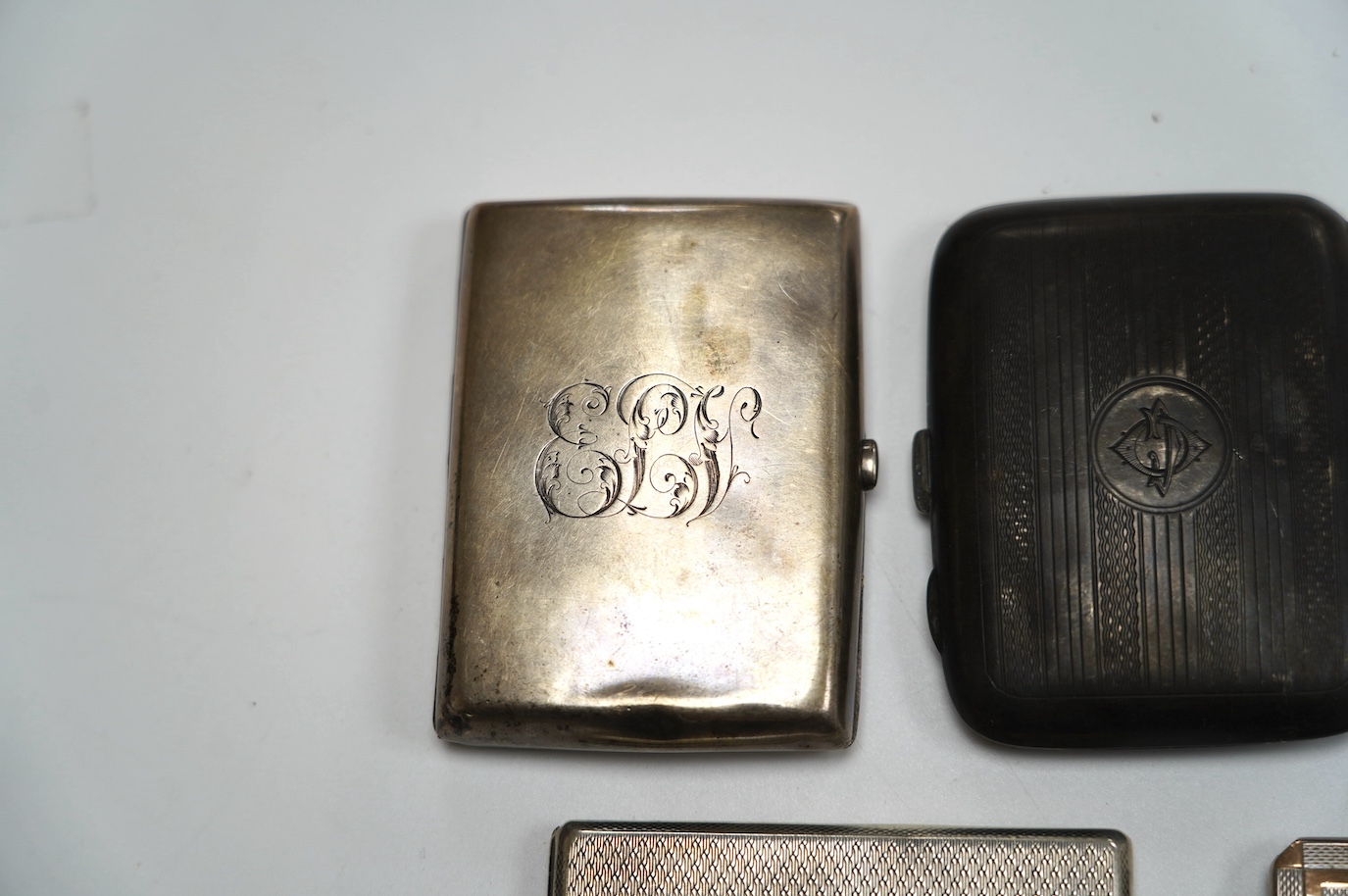 A George VI engine turned silver cigarette case, with yellow metal band, London, 1938, 11.4cm, four other silver cigarette cases and a silver ashtray, gross weight 16.8oz. Condition - poor to fair